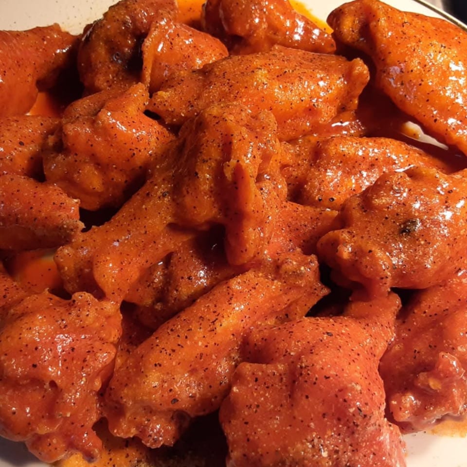 Close-up of Magic Wings & Things' orange-sauced chicken wings, generously seasoned with black pepper.