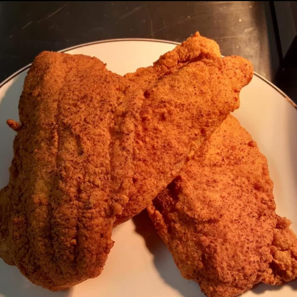 Two crispy, golden-brown fried chicken wings, seasoned with spices, on a white plate.