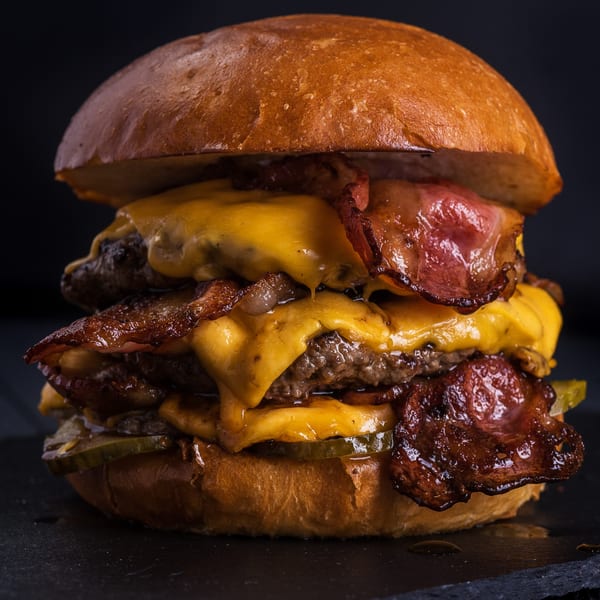 A towering double cheeseburger from Magic Wings & Things, loaded with melted cheese, crispy bacon, and pickles.