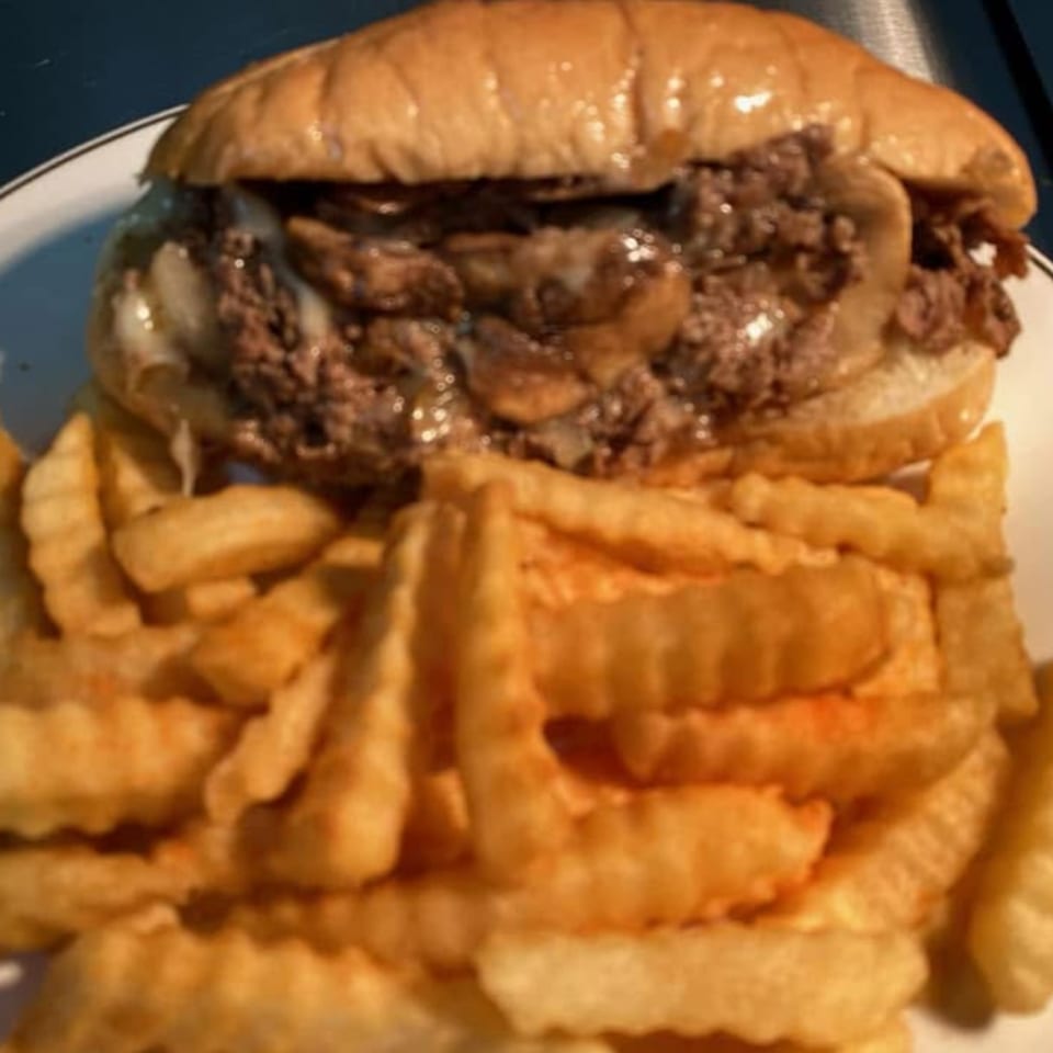 A cheesesteak sandwich with mushrooms and onions, served with a side of crinkle-cut fries.