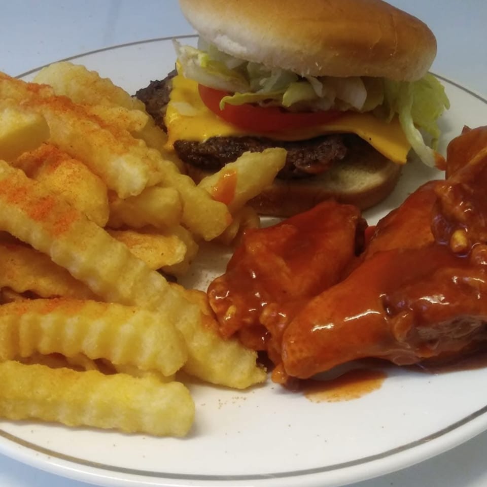 A plate of crinkle-cut fries, a cheeseburger with lettuce and tomato, and saucy chicken wings.