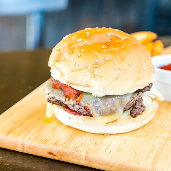A Magic Wings & Things bacon cheeseburger with melted cheese and a sesame seed bun on a wooden board.